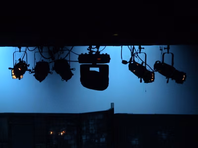 Lighting truss hanging in a theater with (from left to right) a Source 4 ERS, 2 Lekolite ERSs, a Martin MAC 550, and 2 more Source 4 ERSs. THe blue background is due to the cyc being lit with a night blue color gel. The cluser of 3 small lights at the bottom is a street light for the show that was running at the time the picture was taken.
